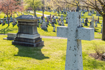 Many headstones in a cemetery with a cross in the foreground