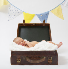 Newborn baby lying in a brown vintage suitcase on a white blanket sleeping