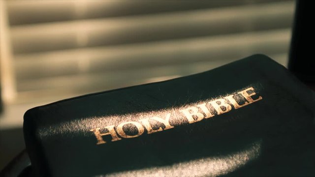 Sunlight filters through window shades and casts a beam of light on the page of an open Bible.