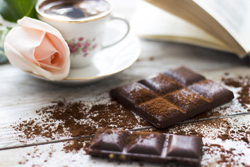 Turkish coffee with peach-colored rose, slices of chocolate and book on the wooden table 