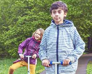 Boy and a girl riding on the scooters in the park