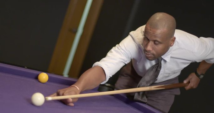 African American business man relaxes by playing pool in a bar lounge setting.  Focus on the cue ball and recorded in slow motion at 60fps.