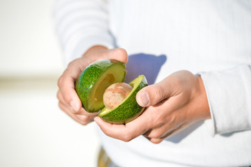 Hands holding fresh avocado cut in half on light background. Closeup 