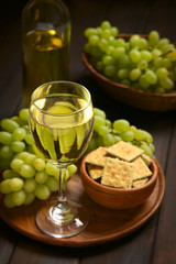 Weisswein in Glas mit Trauben und Kräcker an der Seite, fotografiert mit natürlichem Licht (Selektiver Fokus, Fokus auf den vorderen Glasrand)