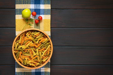 Rohe bunte Fusilli oder Spirelli Pasta in Holzschüssel, fotografiert auf dunklem Holz mit...