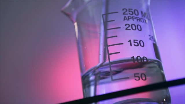 A clear solution in a glass chemistry beaker being stirred or mixed by hand using a glass stir wand.