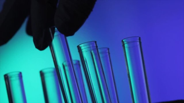 The gloved hand of a technician adds test tubes to a holder