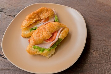 Fresh croissant with ham cheese and salad leaf with fresh salad in dish on wooden texture - France food