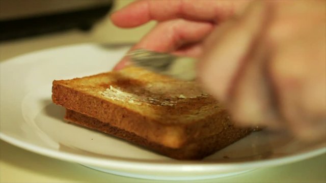 Close up of a man applying butter to a piece of toas