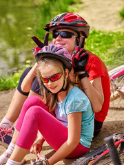 Obraz premium Bikes bicycling family. Happy mother and daughter rides bicycle. Family have rest near water in park. Bicycles are on coast. Little girl looks at camera.
