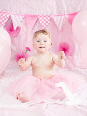 Obraz na płótnie Canvas Portrait of cute adorable Caucasian baby girl with blue eyes in pink tutu skirt celebrating her first birthday with flower, gourmet cake and balloons looking in camera, cake smash first year concept