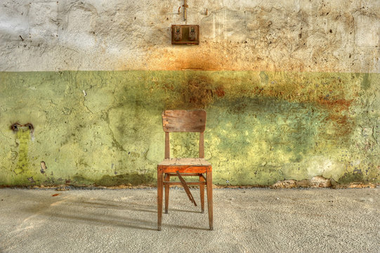 Broken wooden chair against a filthy wall in an abandoned prison.