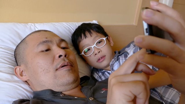 Asian Father and his child playing with smart phone in bed 