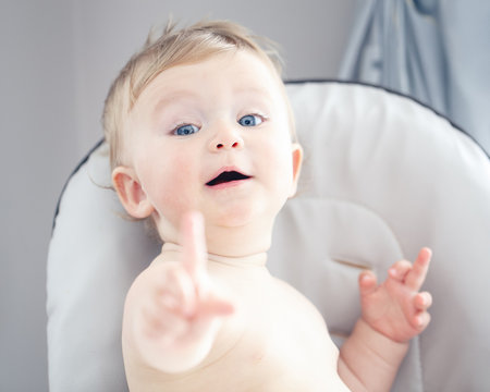 Closeup portrait of cute adorable funny blonde Caucasian smiling laughing baby boy girl with blue eyes with emotional face expression showing one finger