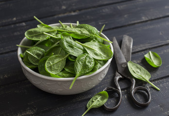 Fresh spinach in a white bowl  and old vintage scissors on a dark wooden background. Healthy food