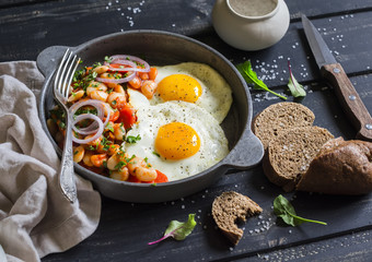 Fried egg, beans in tomato sauce with onions and carrots, fresh cucumbers and tomatoes, homemade rye bread - delicious  breakfast or snack  on dark wooden background