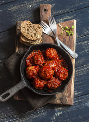 Meatballs in tomato sauce in a cast iron skillet on a wooden rustic board on a dark background