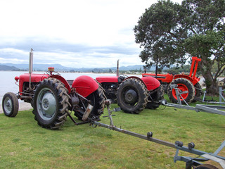 Obraz premium A row of old red tractors on a beach, ready for recovering fishing boats from the sea. Photographed at Whitianga, Coromandel Peninsula, New Zealand.