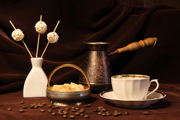 Coffee grinder, cup on the table. Brown background, still-life, tableware. Drinking coffe, book. Cezve, Ibrik brewing coffee oriental ornaments form ancient oriental emblem, dried fruits. Silver 