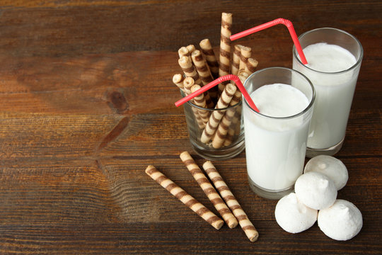 a milkshake with a cocktail straw near the glass with cookies on wooden background