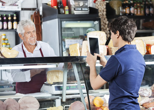 Man Photographing Salesman Packing Cheese In Shop - Powered by Adobe