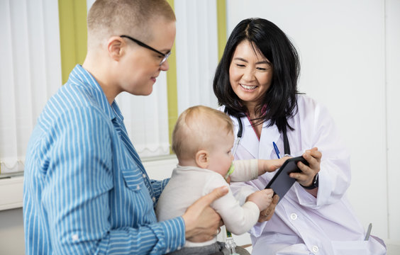 Woman Looking At Baby Grabbing Digital Tablet From Female Doctor
