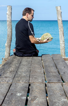 A man sits on a pier with a noose around his neck