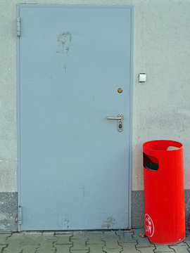 Red garbage can in front of a dirty door