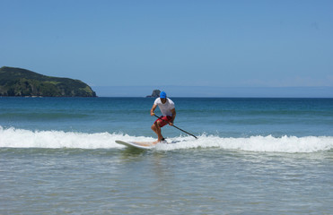Paddleboarder on a SUP surfing a wave. Paddle boarder photographed in Northland, New Zealand.