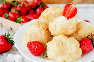
dessert with berries , custard eclairs or cakes with cream and red strawberries on a wooden background
