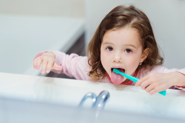 Little girl in pink pyjamas in bathroom brushing teeth