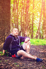 Hiker, young man has dreamy look, resting under the tree in beautiful forest, outdoors summertime journey concept