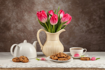 Tulips in a vase, tea, chocolates on the board