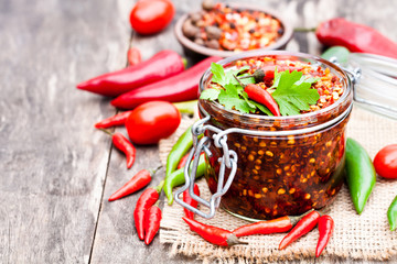 Red  hot chili peppers marinated in a glass jar on wooden backgr