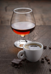 Cup of coffee, cognac glass and coffee beans on a wooden table