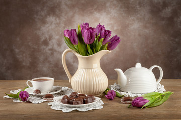 Tulips in a vase, tea, chocolates on the board.