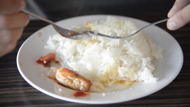 Asian man eating the rice and Thai spicy shrimp soup (Tom Yum Kung) with spoon and fork closeup on the dish closeup.