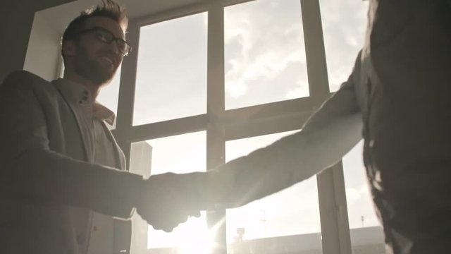 Two businessmen shaking hands to greet each other and talking near window in office, backlit slow motion shot on Sony NEX 700    