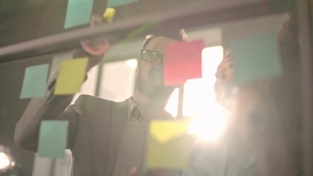 Young business team brainstorming and writing down ideas on sticky notes attached to glass wall, shot on Sony NEX 700    