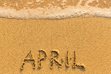 April - written by hand on a golden beach sand.