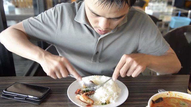 Asian man eating the rice and Thai spicy shrimp soup (Tom Yum Kung) with spoon and fork closeup on the dish closeup