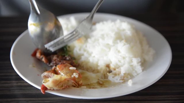 Asian man eating the rice and Thai spicy shrimp soup (Tom Yum Kung) with spoon and fork closeup on the dish closeup.