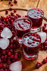 Cold cranberry drink in glasses, cranberries and pieces of ice on wooden background.