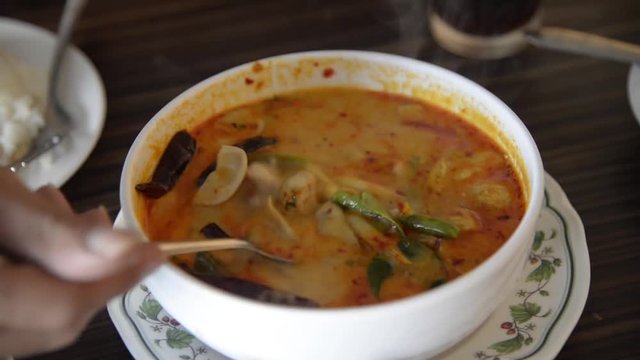 Asian man spoon the hot Thai spicy shrimp soup (Tom Yum Kung) from bowl with smoke