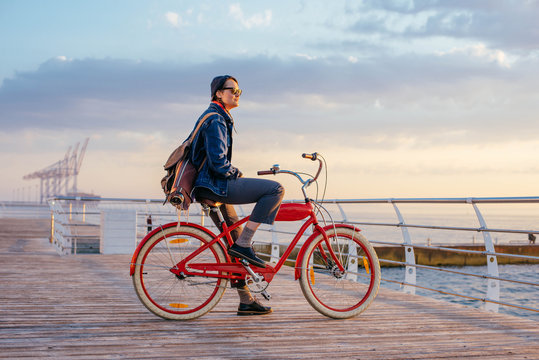 woman with vintage bicycle looking at view on seaside during sunset or sunrise