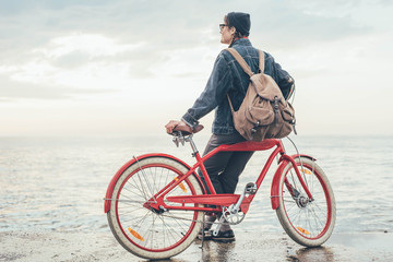 woman with vintage bicycle looking at view on seaside during sunset or sunrise