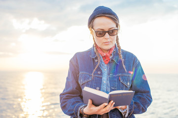 young woman with vintage bicycle resting and reading a book on seaside