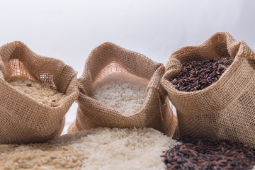 Three sack with different types of rice: brown rice, riceberry rice and white (jasmine) rice on white background. Selective focus