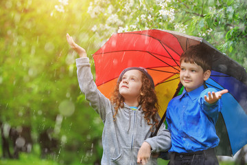 Children under umbrella enjoy to spring rain outdoors.