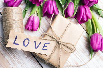 word LOVE and bouquet of tulips on wooden background